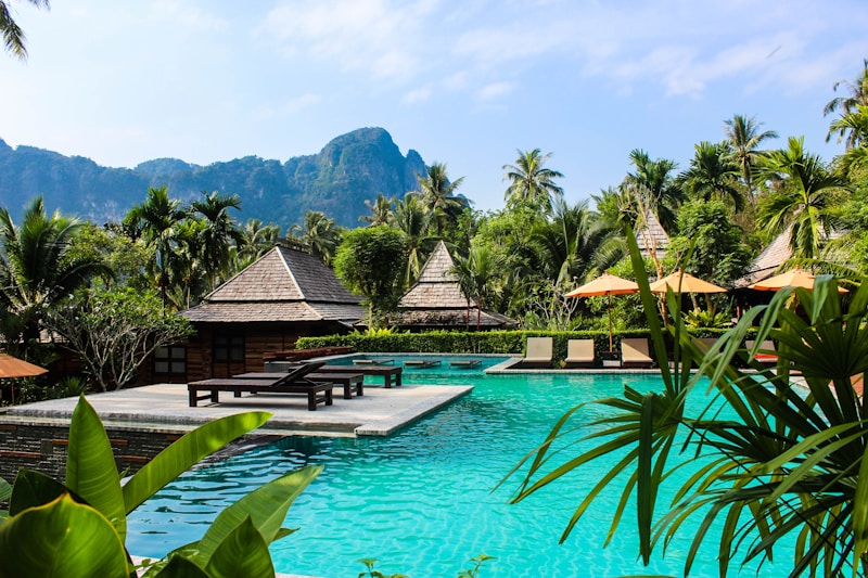 Tropical wellness resort with turquoise pool, wooden villas, palm trees, and mountain backdrop
